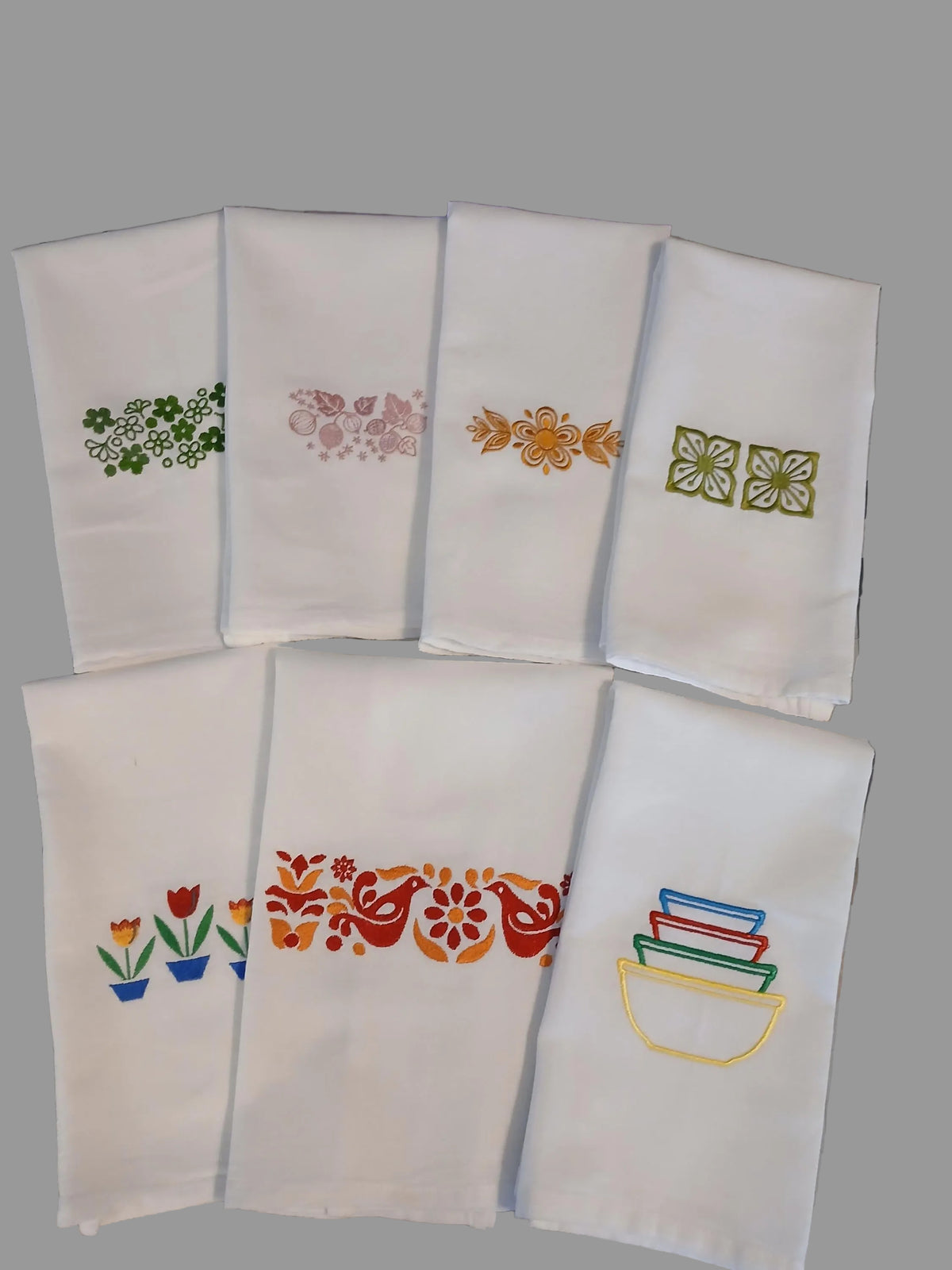 Six white embroidered kitchen towels, each featuring different colorful floral and geometric embroidery designs inspired by Pyrex patterns.