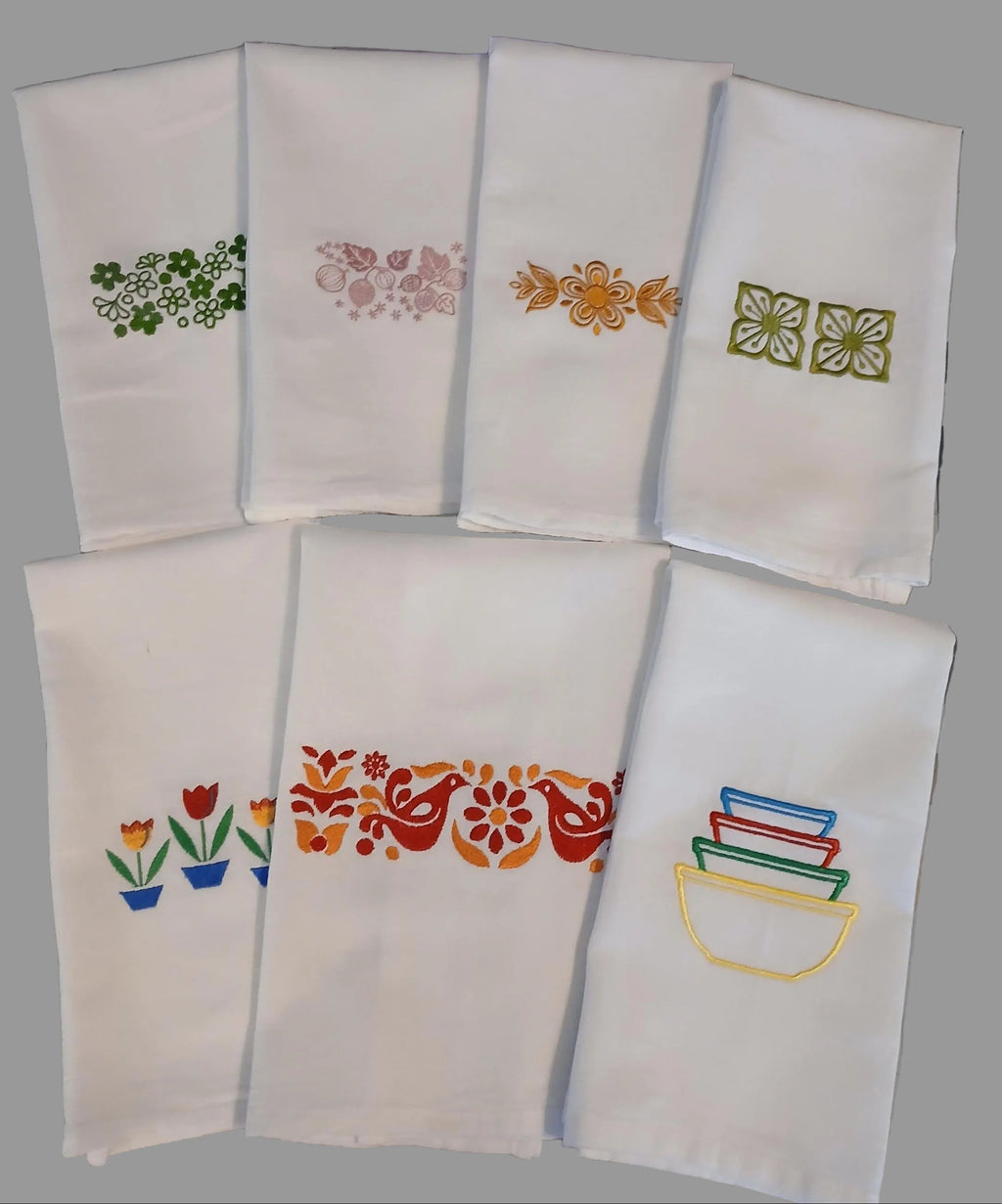 Six white embroidered kitchen towels on a gray background, each featuring different colorful floral and geometric embroidery designs.