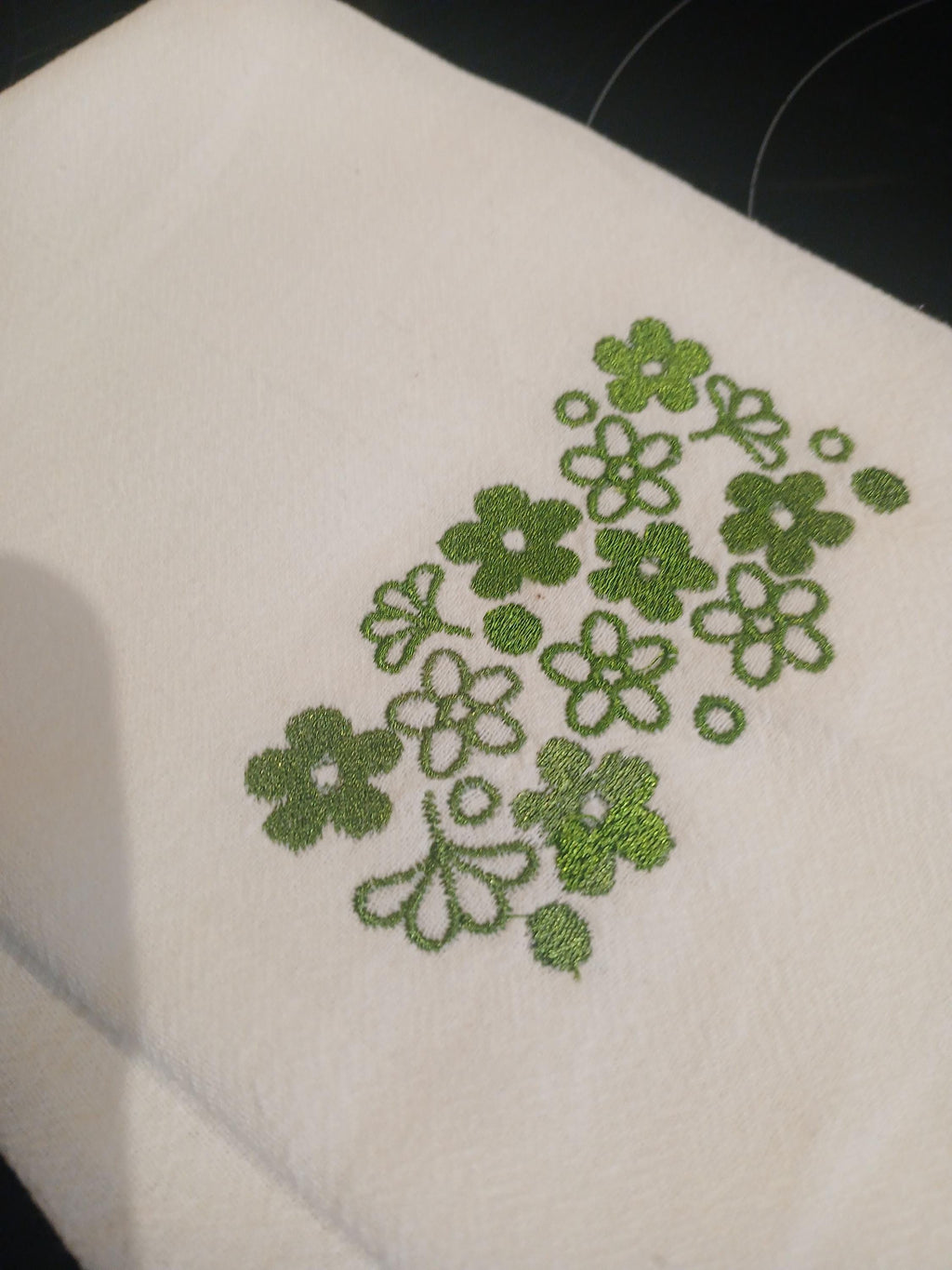 A close-up a white kitchen towel, with an embroidered green floral pattern.