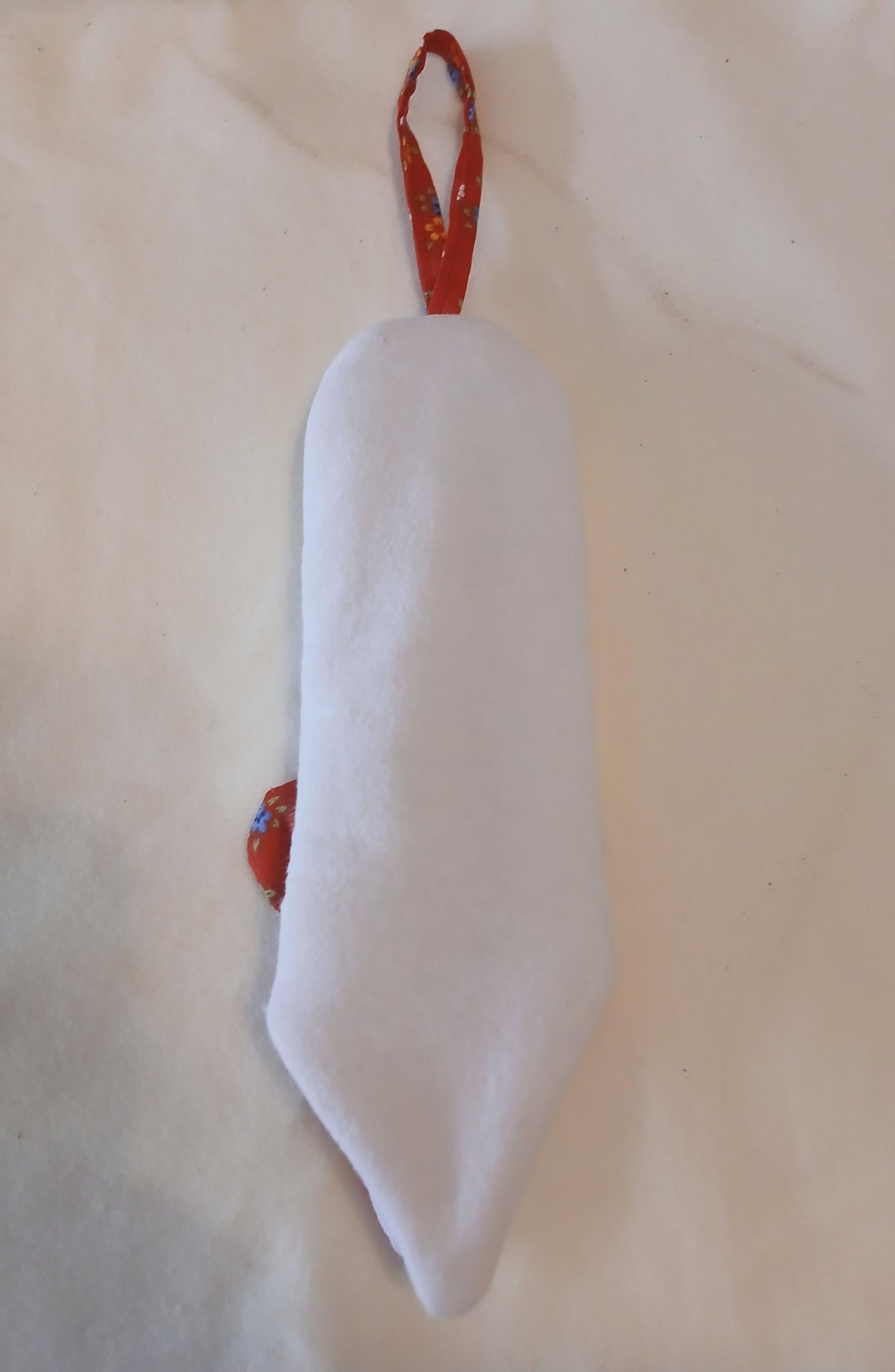 The white back of a handle potholder, with a red patterned hanging loop, photographed on a light cream fabric background.