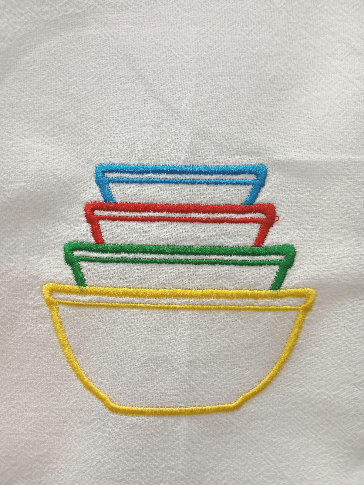 A close-up of embroidered stacked bowls in yellow, green, red, and blue on white fabric.