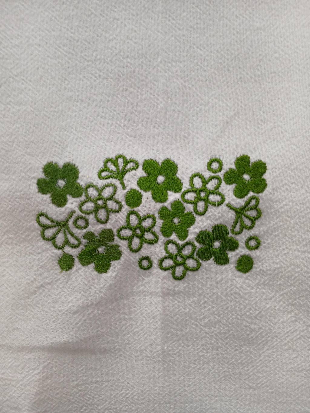 Green embroidered floral pattern on a white textured fabric background.


