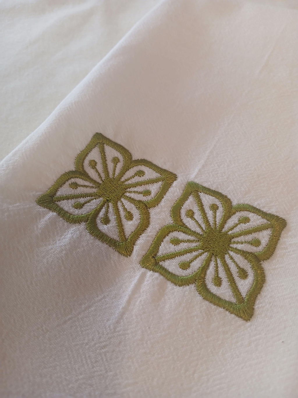 A close-up of a white kitchen towel, featuring two embroidered green floral motifs.