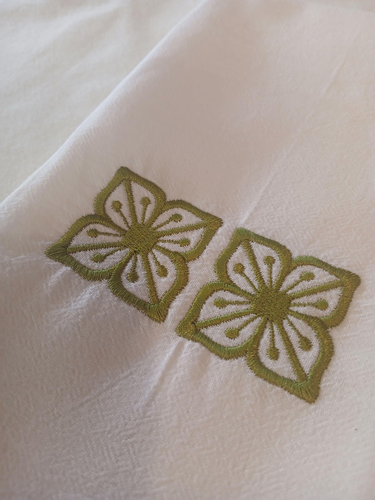A close-up of a white kitchen towel, featuring two embroidered green floral motifs.