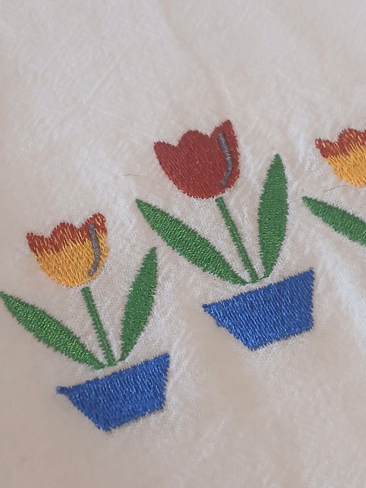Close-up of embroidered tulips in blue pots on a white fabric background.