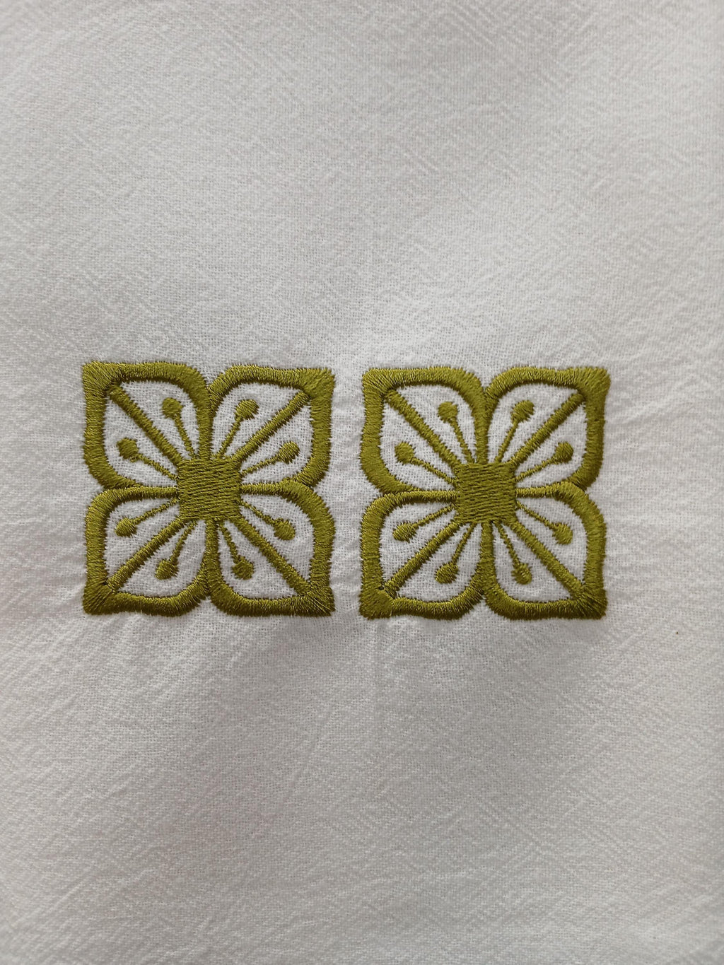 Two matching embroidered square designs with a stylized floral cutout design in olive green thread on a white textured fabric background.