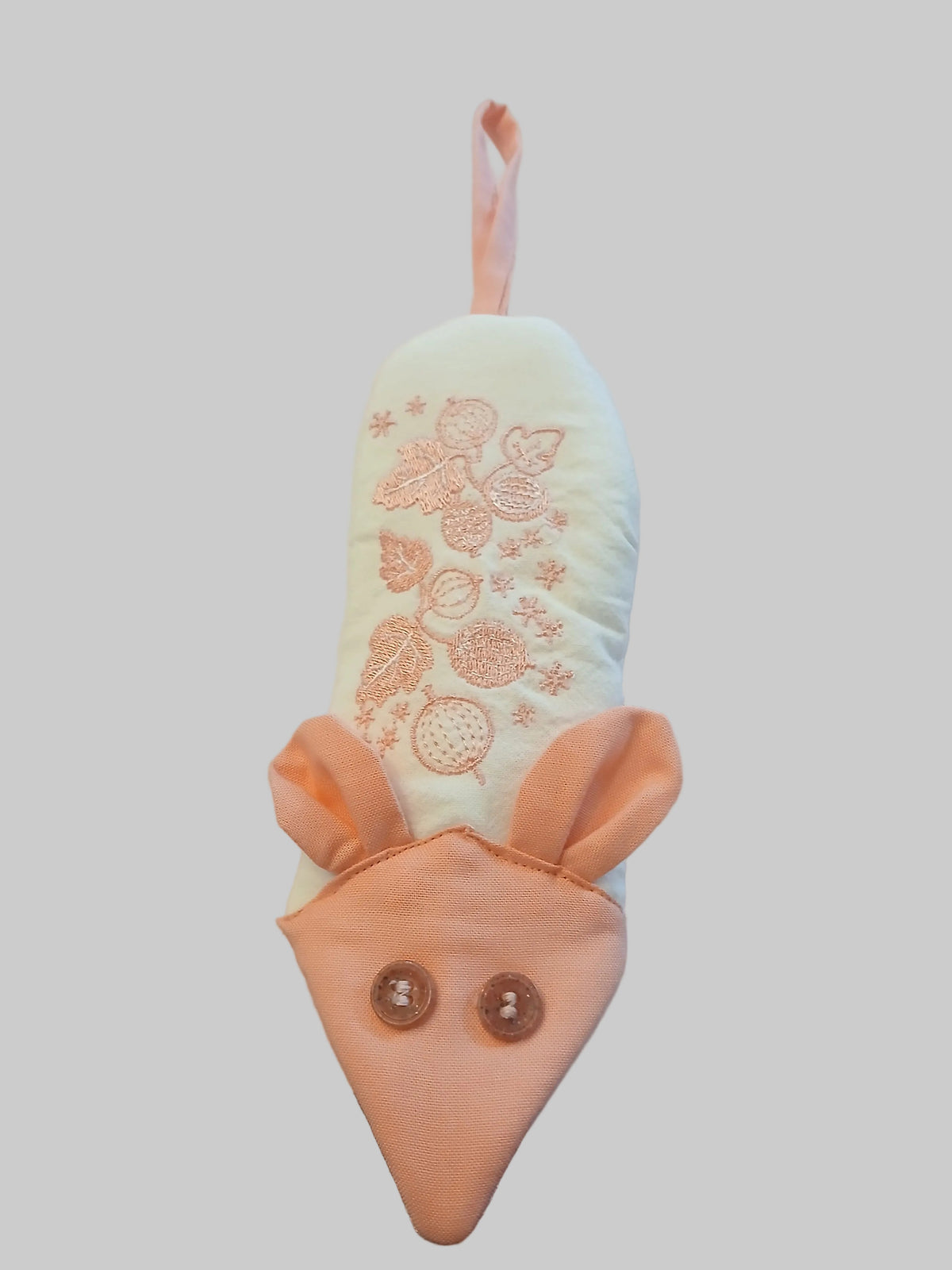 A handmade mouse-shaped fabric oven mitt with a white body, pink ears and tail, and embroidered floral details, resting on a white fabric background.